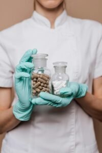 Close-up of a healthcare worker holding bottles of capsules and tablets wearing gloves.